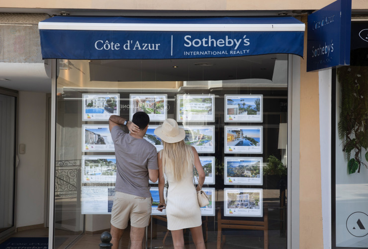 Минувачи разглеждат обяви за имоти на витрината на офис на Sotheby&#39;s в Сен-Жан-Кап-Фера. Фотограф: Andrey Rudakov/Bloomberg